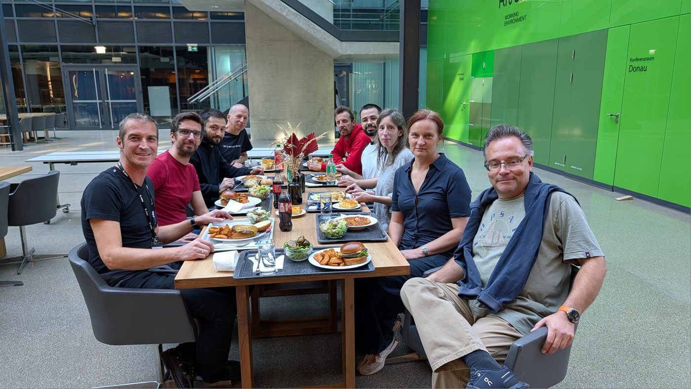 Das Team der Barcodesystems 26 GmbH beim gemeinsamen Mittagessen an einem langen Tisch im Atrium des Rivergate in Wien